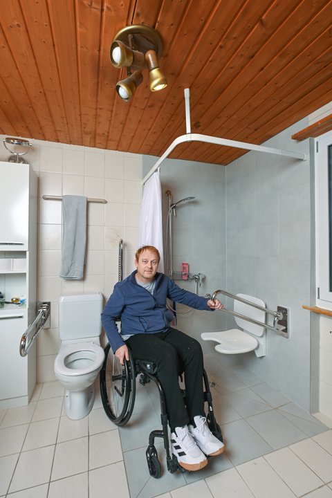 Une personne en fauteuil roulant est assise devant une douche sans obstacle dans la salle de bain.
