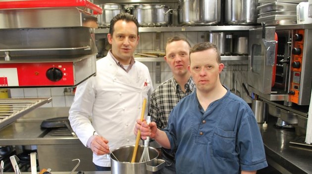 Zwei junge Männer mit Behinderungen unterstützen einen Koch in der Küche