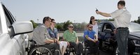 Eine Gruppe Rollstuhlfahrer wird von einem Instruktor ins Autofahren eingeführt 