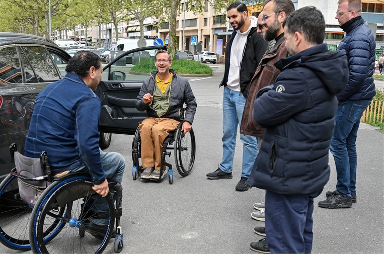 Deux personnes en fauteuil roulant, debout devant une voiture, discutent avec des chauffeurs de taxi