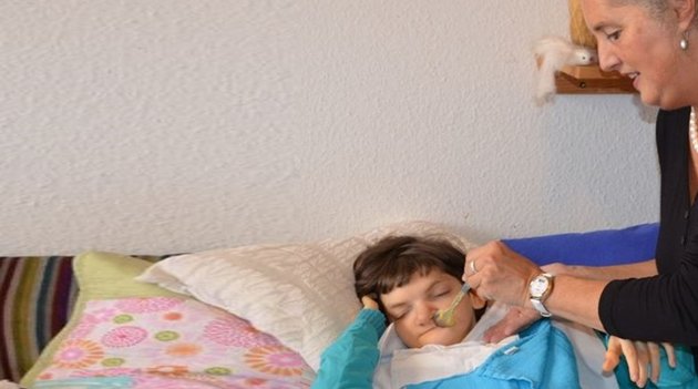 Une mère nourrit sa fille atteinte d'un lourd handicap dans son lit.