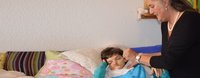 Eine Mutter gibt ihrer kleinen Tochter, die im Bett liegt, das Essen ein.