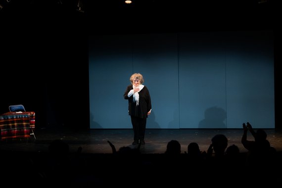 Sur scène une femme debout salue le public une main posée sur son coeur.