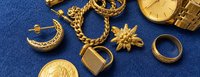 Verschiedene Altgold-Schmuckstücke, eine goldene Armbanduhr und eine Helvetia-Goldmünze auf blauem Untergrund.