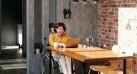 Eine junge Frau sitzt im Wohnzimmer und arbeitet am Computer
