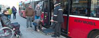 Ein Mann hat die Rampe bei einer Türe eines Busses ausgeklappt, damit der Rollstuhlfahrer aussteigen kann.