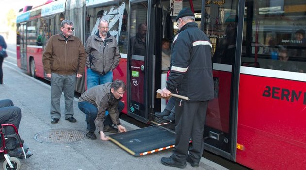 Un homme aide une personne en fauteuil roulant à descendre d'un bus à l'aide d'une rampe..
