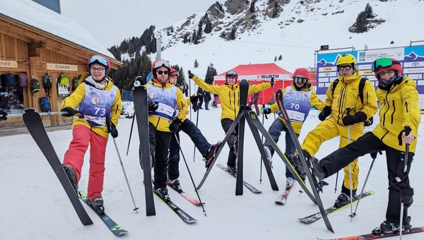 Des skieurs vêtus de combinaisons jaunes sont alignés et lèvent leur ski droit.