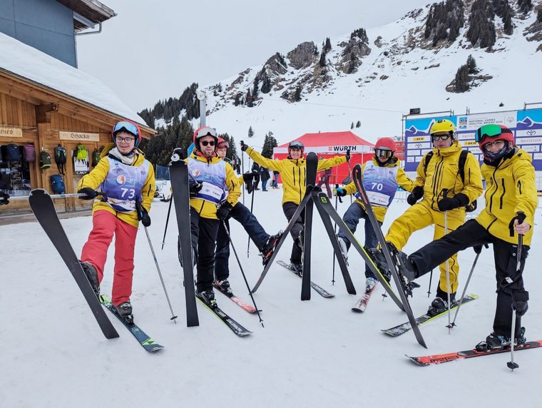 Des skieurs vêtus de combinaisons jaunes sont alignés et lèvent leur ski droit.