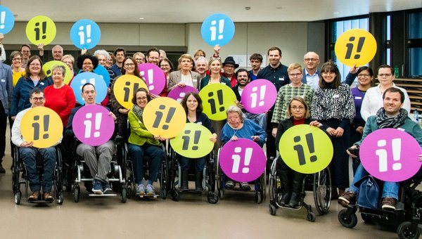 Menschen mit und ohne Behinderungen, die das Logo der Inklusionsinitiative in die Luft halten