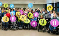 Menschen mit und ohne Behinderungen, die das Logo der Inklusionsinitiative in die Luft halten