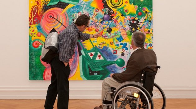 Deux hommes, dont un en fauteuil roulant, regardent une image avec beaucouo de couleurs.