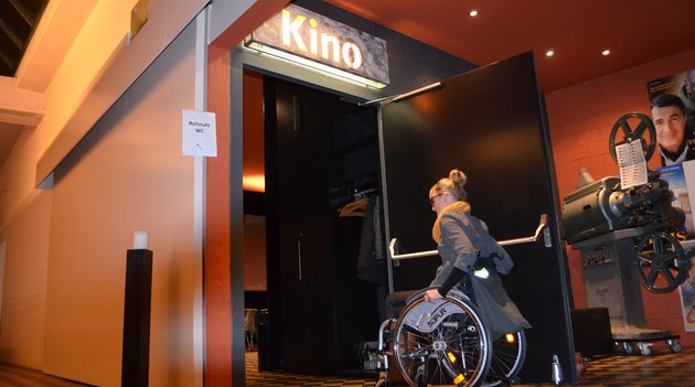 Frau im Rollstuhl fährt durch barrierefreien Kinoeingang 