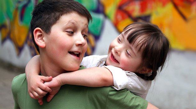 Un garçon porte une fillette atteinte de trisomie 21 sur son dos. Ils sont heureux et échangent un regard rayonnant. 