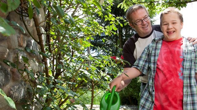 Père et fils arrosant ensemble des fleurs dans un jardin