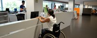 Eine Frau sitzt im Rollstuhl vor einem Schalter eines Büros.