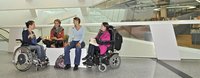 Vier junge Frauen, zwei davon im Rollstuhl, diskutieren in einem Einkaufszentrum