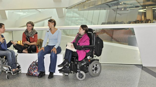 Vier junge Frauen, zwei davon im Rollstuhl, diskutieren in einem Einkaufszentrum