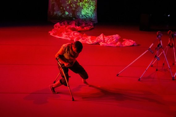 Eine Tänzerin mit Krücken auf einer rot beleuchteten Bühne