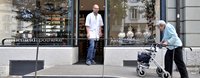 Eine Frau mit Rollator geht via Rampe in einer Apotheke einkaufen