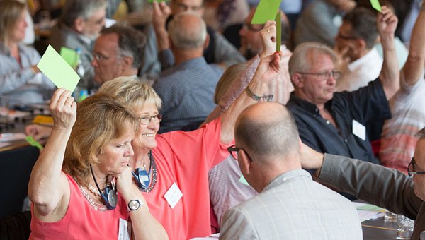 Des participants d'une assemblée generale lèvent la carte de vote.