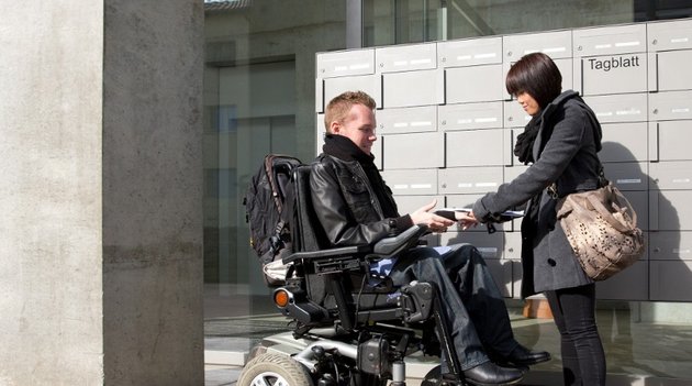 Ein Mann im Rollstuhl wird von einer Assistenz unterstützt.
