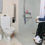 Ein Rollstuhlfahrer präsentiert sich stolz in seinem angepassten Badezimmer mit bodenebener Dusche