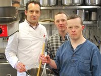 Zwei Männer mit Behinderung und ein Mann ohne Behinderung in einer Küche