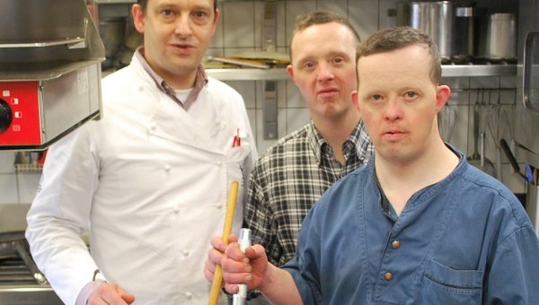 Zwei Männer mit Behinderung und ein Mann ohne Behinderung in einer Küche