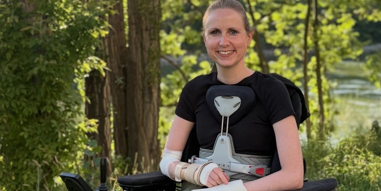 Céline est assise dans un fauteuil roulant électrique lors d'une promenade en forêt