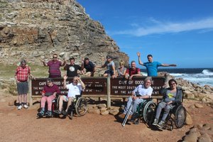 Un groupe de personnes en fauteuil roulant accompagnées de leurs accompagnateurs sur une côte rocheuse au bord de la mer