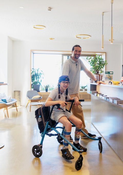 Une jeune fille à mobilité réduite, vêtue de ses habits de vacances, est assise sur son déambulateur