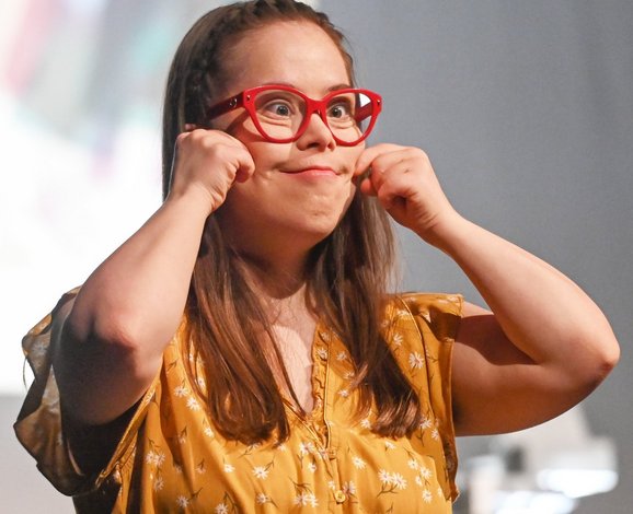 Eine junge Frau mit roter Brille macht eine Grimasse